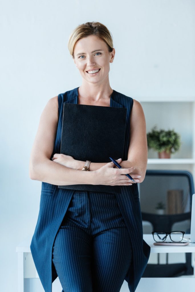 happy adult businesswoman holding folder and pencil near table in office